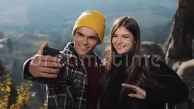 恋爱中的年轻夫妇站在山上的一块岩石上，和朋友视频聊天。 旅游、交流